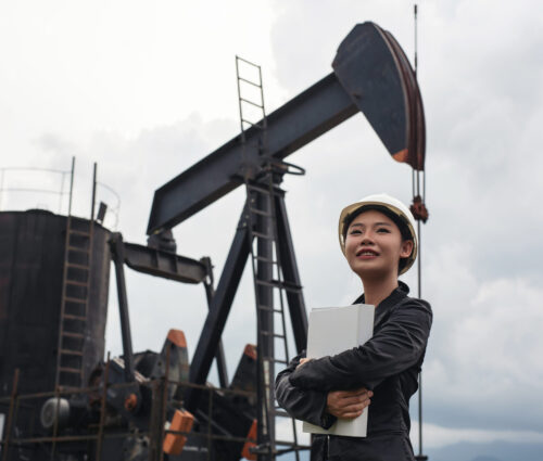 Female engineer standing beside working oil pumps with a sky background.