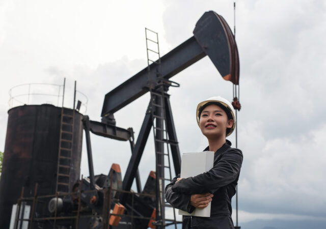 Female engineer standing beside working oil pumps with a sky background.