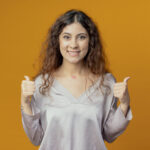 smiling young pretty girl her thumb up isolated on yellow background